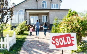 Family walking down sidewalk toward new house, sold sign in foreground