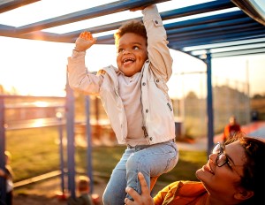 Mother helping smiling little boy playing on a jungle gym